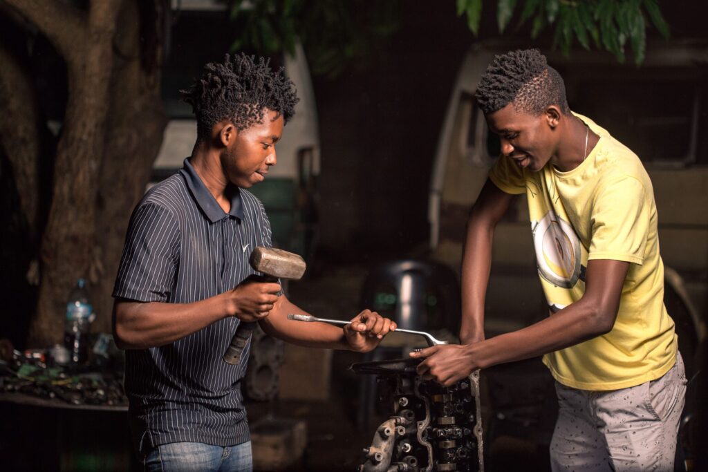 Two young mechanics working on a car engine outdoors in Mozambique.